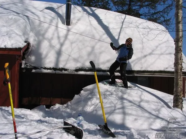 Человек убирает снег с крыши при помощи веревки