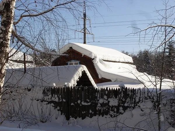 Частный дом за забором зимой, занесенный снегом