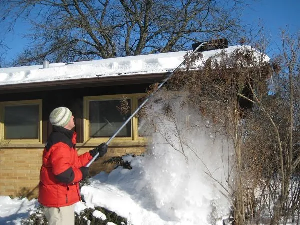 Человек убирает снег с крыши специальным скребком с длинной ручкой